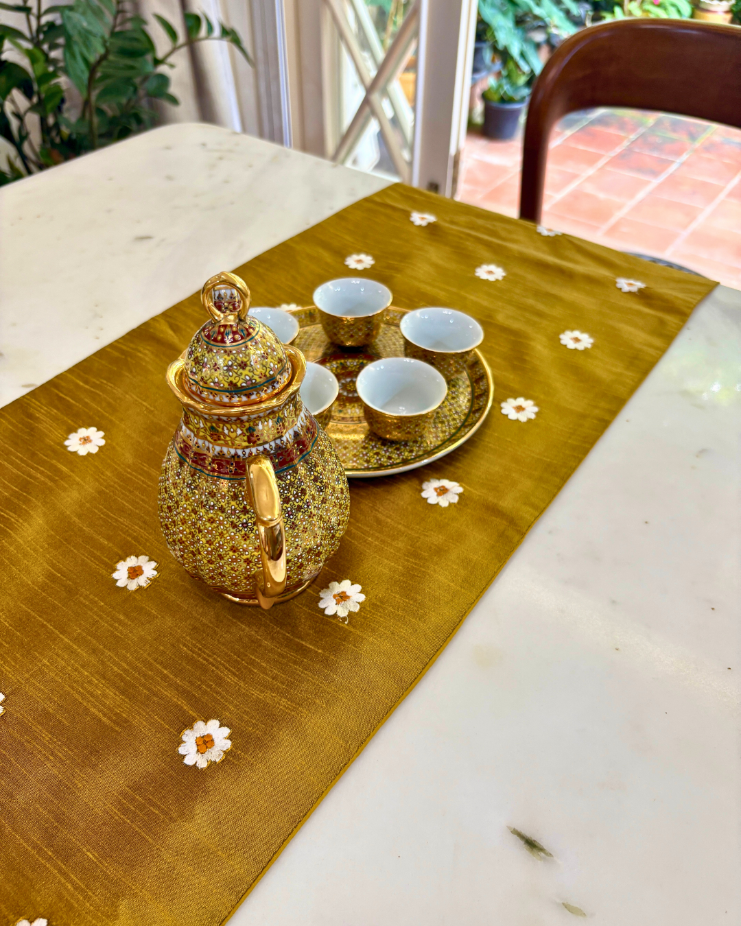Decorative tea set with a teapot and cups on a table with a floral runner.