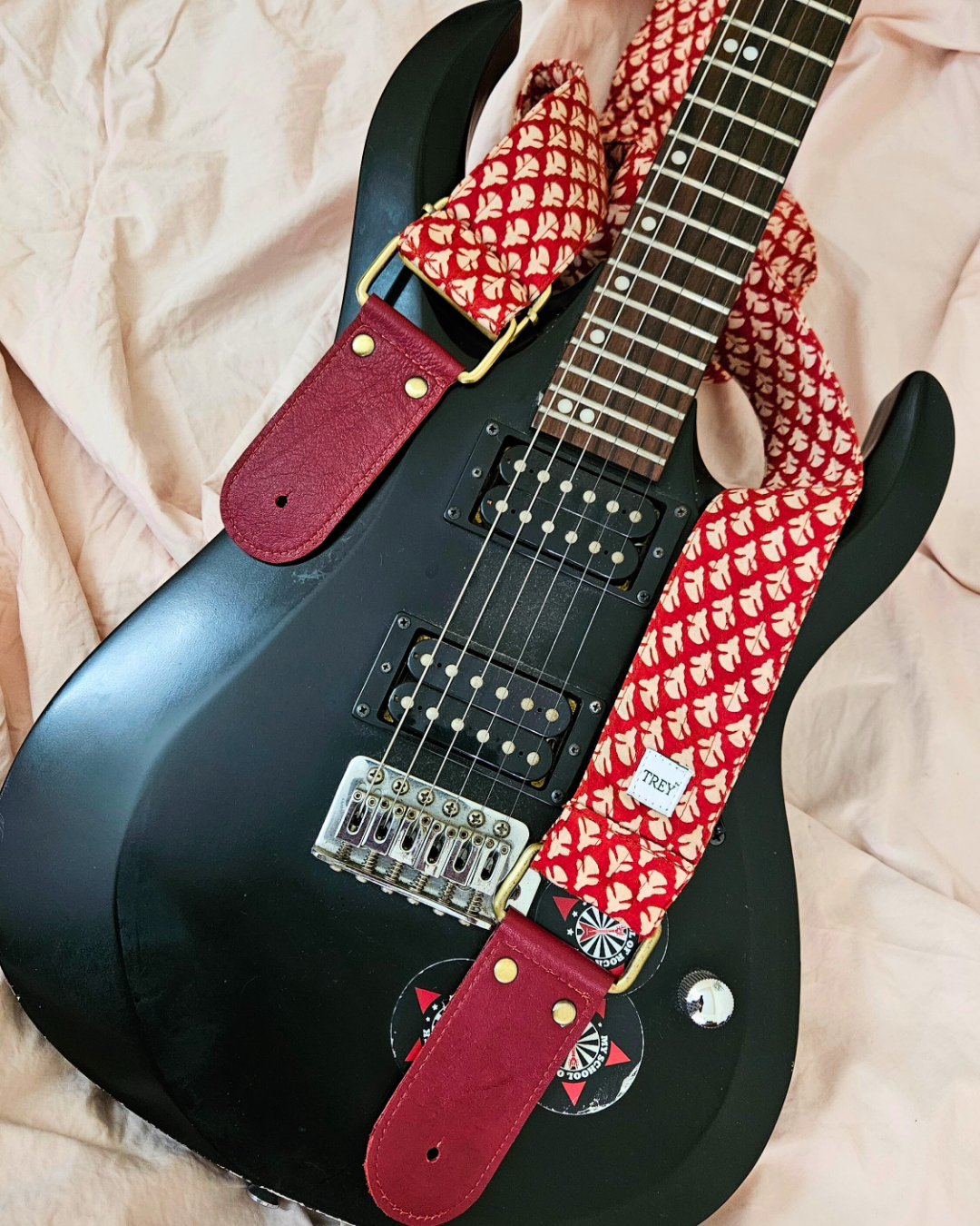 Black electric guitar with a red and white patterned guitar strap 